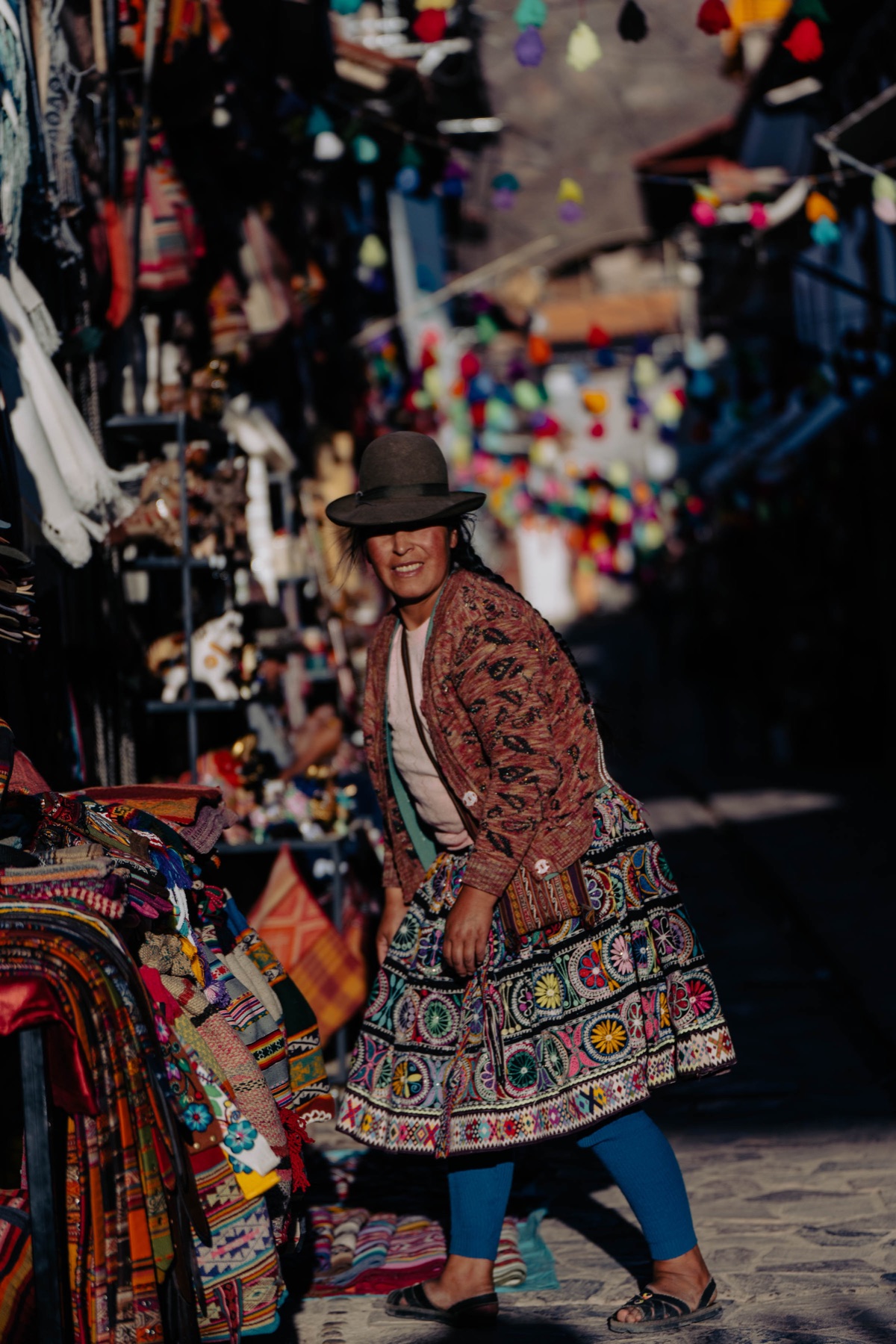 Mujer con vestimenta tradicional entre textiles y artesanías en el mercado de Pisac.
