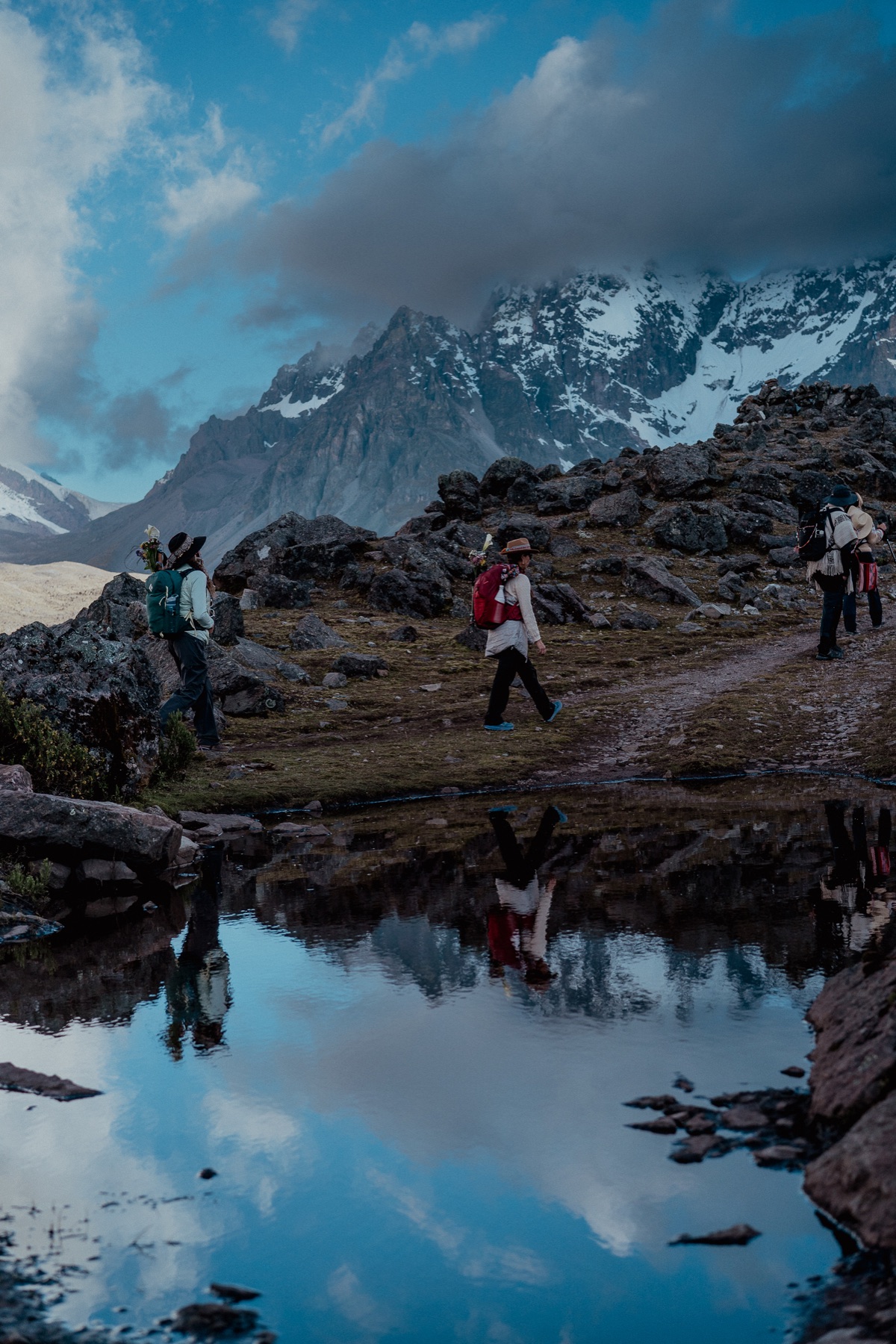 Peregrinos caminan junto a una laguna que refleja las montañas del Ausangate.