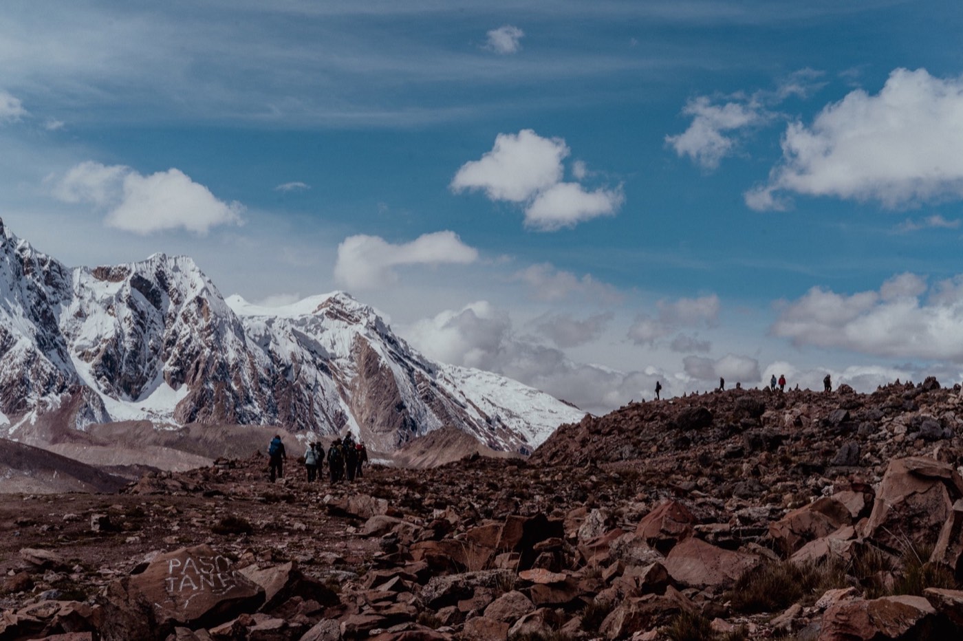 Peregrinos atraviesan un paso rocoso con la cordillera nevada al fondo.