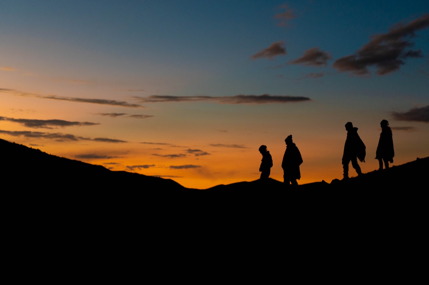 Siluetas de caminantes atraviesan la montaña durante el atardecer.