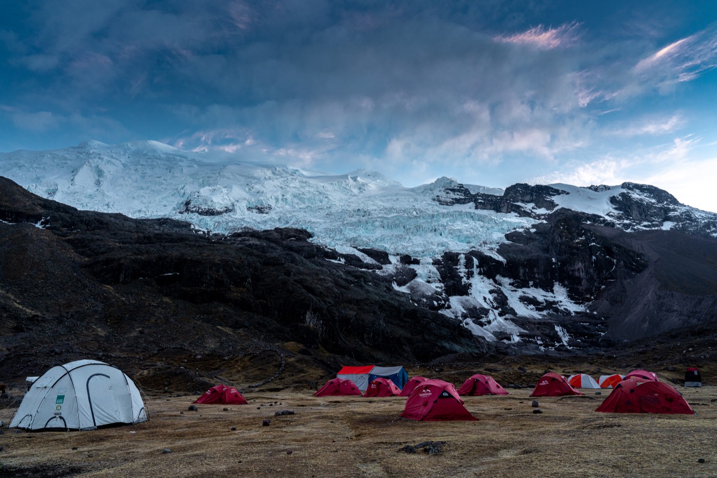 Campamento de tiendas rojas instalado bajo un extenso glaciar.
