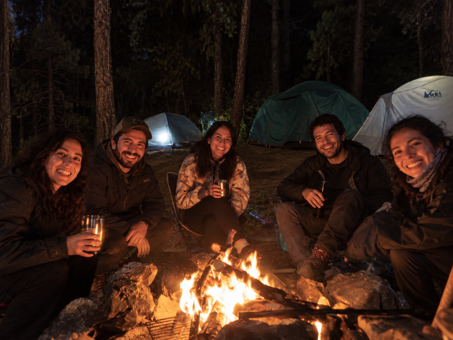 Participantes comparten una fogata en el campamento entre los árboles.